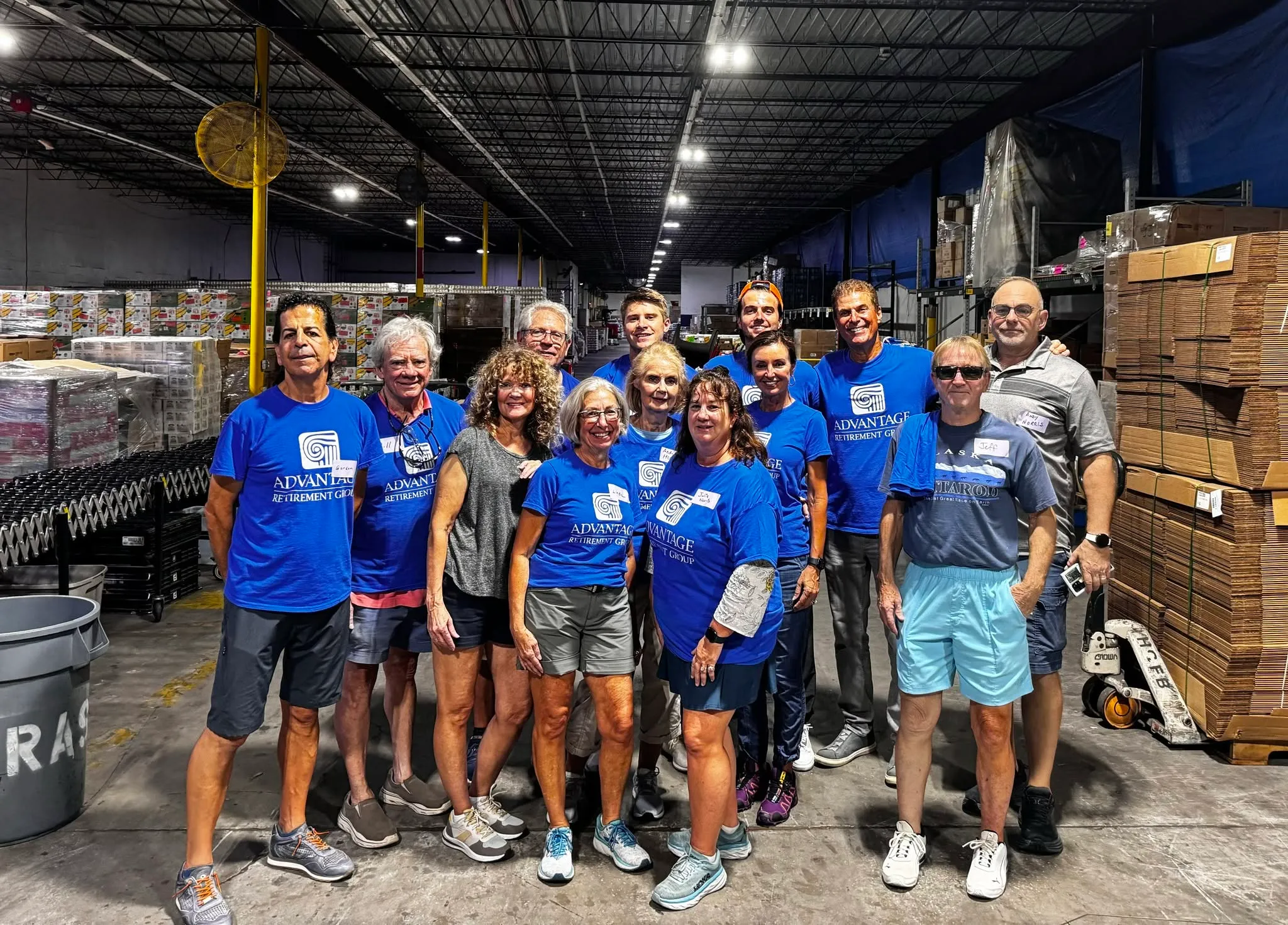 Volunteers from Advantage Wealth Partners and friends standing together in a food bank warehouse, pallets of boxed food stacked behind them