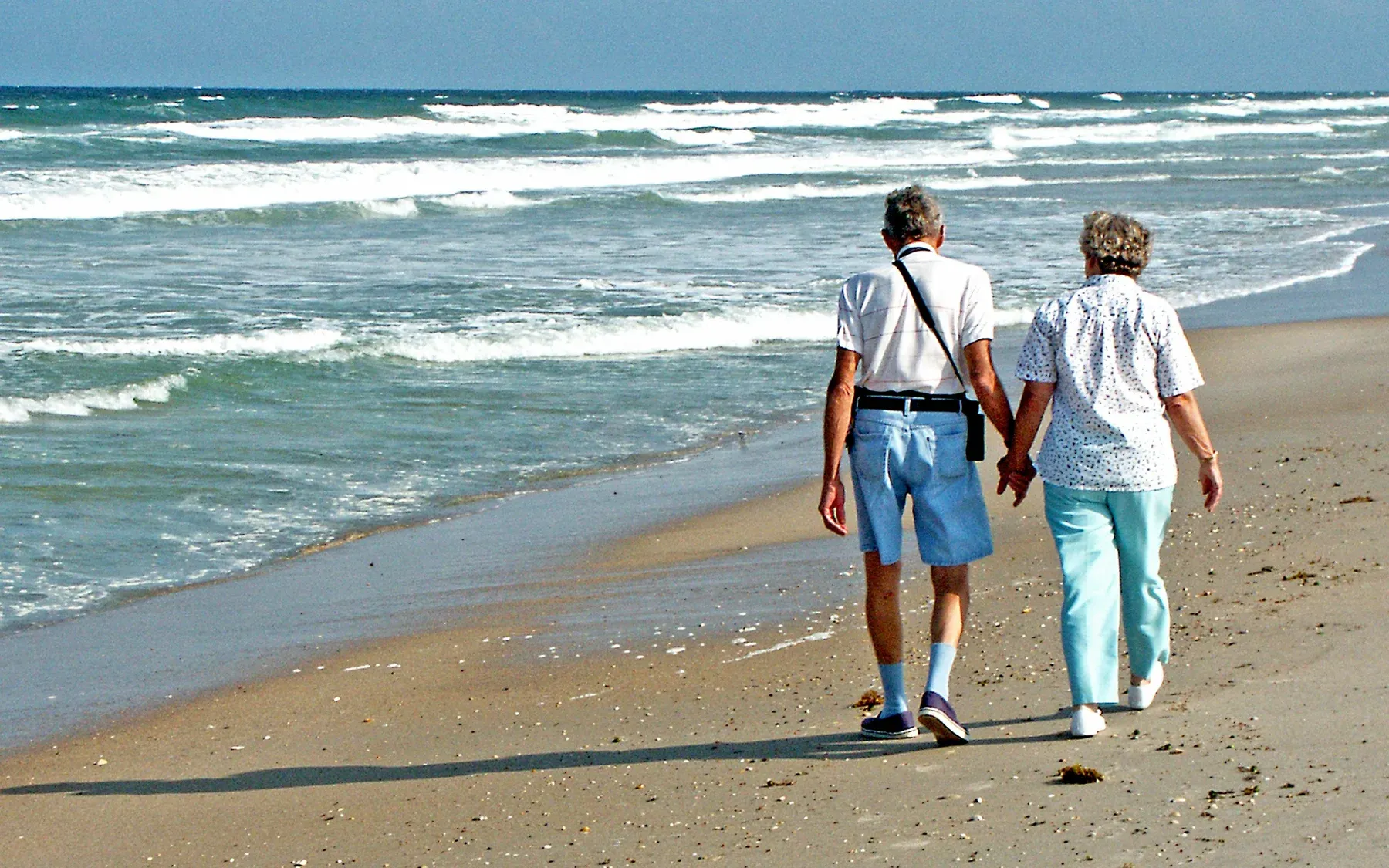 An older couple walking hand in hand along the beach at the water's edge